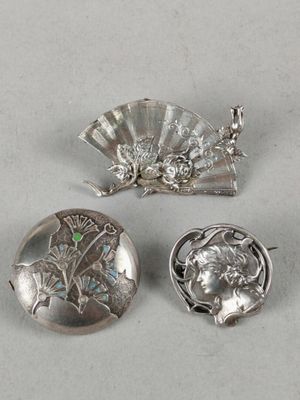 three silver brooches and a fan on a white surface