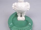 a white figurine of a man on top of a green ashtray