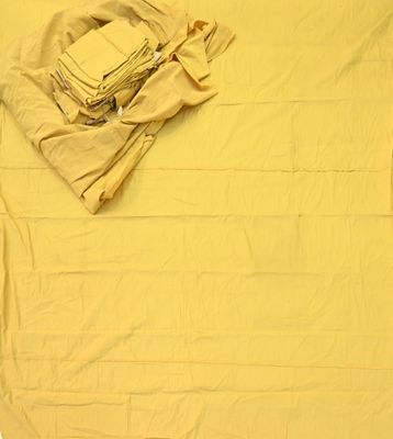 un lit avec une couverture jaune et une pile de vêtements pliés