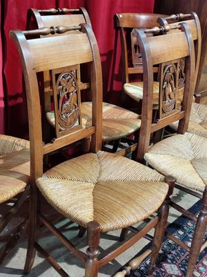 Quatre chaises en bois avec des assises en osier sont disposées devant un rideau rouge