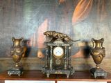 une horloge et deux vases posés sur une étagère devant un tableau