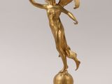 gold statue of a woman holding a fan on top of a ball