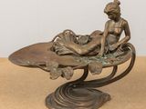 bronze statue of a woman sitting on a leaf shaped bowl