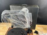 Le tourne-disque est posé sur une table en bois, son boîtier étant emballé dans du plastique.
