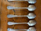 six silver spoons are lined up on a wooden table