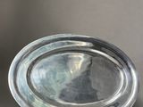 an oval silver plate with a handle on a gray background