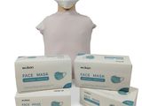 une personne portant un masque à côté de trois boîtes de masques jetables