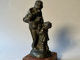 figurine en bronze représentant un homme tenant un enfant dans ses bras, posée sur un socle en bois