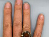 a person ' s hand holding a ring with a brown stone