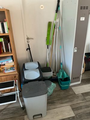 une pièce dans laquelle se trouvent une bibliothèque, une poubelle et un balai