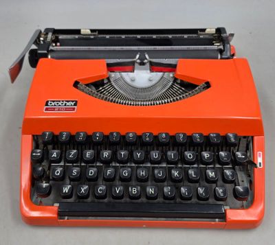 une machine à écrire orange posée sur une table, à côté d'un clavier