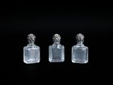 trois bouteilles en verre transparent munies de bouchons argentés sont posées sur une surface noire
