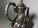an antique silver tea pot with a twisted handle on a gray surface