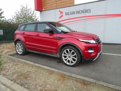 Le Range Rover rouge est garé devant un immeuble.