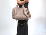 une femme en robe noire, tenant un sac à main beige et regardant son téléphone portable