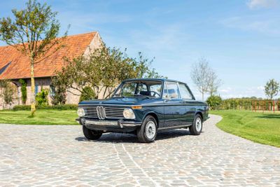 an old black car parked on a cobblestone road in front of a house