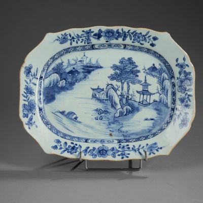 blue and white plate with a landscape scene on it on a stand