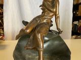 statue en bronze représentant une femme assise sur un rocher posé sur une table