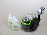un aspirateur vert et noir à côté d'une bouteille de produit nettoyant