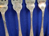six silverware forks are lined up on a blue cloth