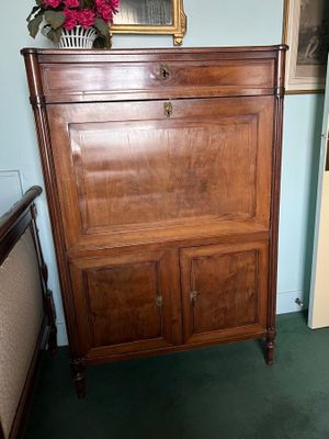 a wooden cabinet in the corner of a room with a painting on the wall