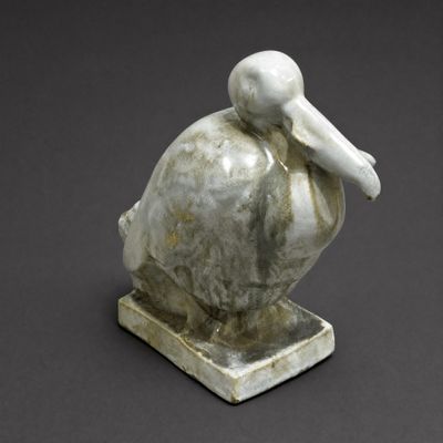statue of a pelican sitting on a base on a gray surface