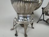 a silver tea pot sitting on a stand next to a chair