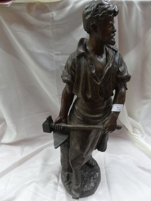 statue en bronze représentant un garçon tenant un marteau, posée sur un tissu blanc
