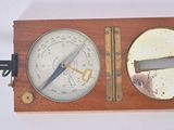 a wooden and metal clock with a barometer on top of it