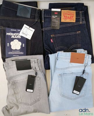 trois paires de jeans pour homme et un téléphone portable posés sur une table