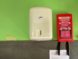 a green wall with a white paper towel dispenser and a red box on it