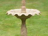 a bird sitting on top of a fountain in the grass