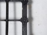 a close up of a black iron fence with a white wall in the background