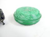 a green glass box with a lid sitting next to a small figurine