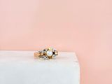 un gros plan d'une bague en or et perles sur fond rose