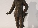 statue d'un homme portant un chapeau et tenant un fusil, posée sur une surface blanche