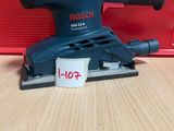 une ponceuse orbitale Bosch posée sur une table, à côté d'une boîte rouge