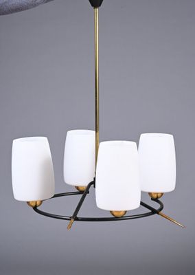un gros plan sur la main d'une personne tenant un lustre muni de cinq abat-jours en verre blanc