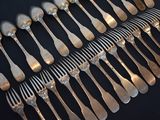 a lot of silver spoons and forks on a black table