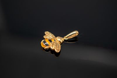 un gros plan d'un pendentif en forme d'abeille dorée sur une surface noire