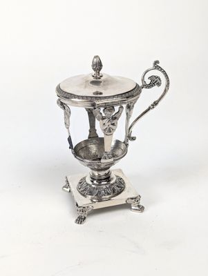 une théière ancienne plaquée argent, posée sur un support, sur fond blanc
