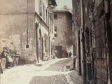 a black and white photo of a narrow street with people sitting on benches