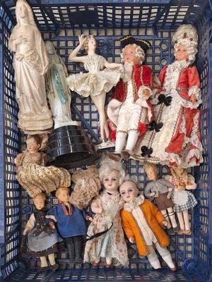 de nombreuses poupées dans un panier bleu, avec une statue en arrière-plan