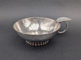 an antique silver bowl with a handle on a black surface
