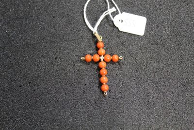 an orange beaded cross hangs from a silver chain on a black surface