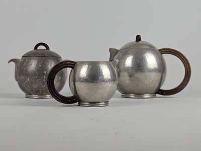 two silver teapots and a coffee pot on a white surface