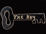 a black and gold key pin with the word the key on it