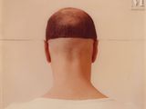 a man with a shaved head standing in front of a white wall