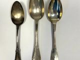 three silver spoons are lined up on a white surface