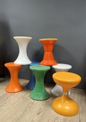 four different colored stools sitting on a wooden floor